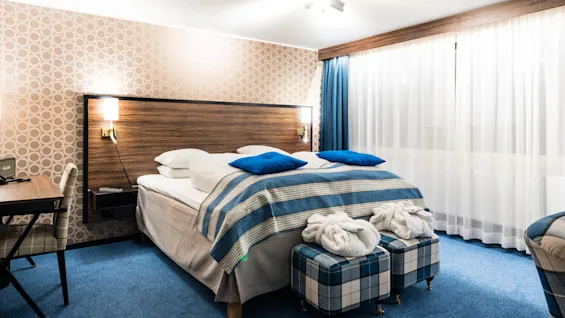 En snyggt bäddad säng med blå och randiga detaljer i ett välbelyst, mönstrat hotellrum.