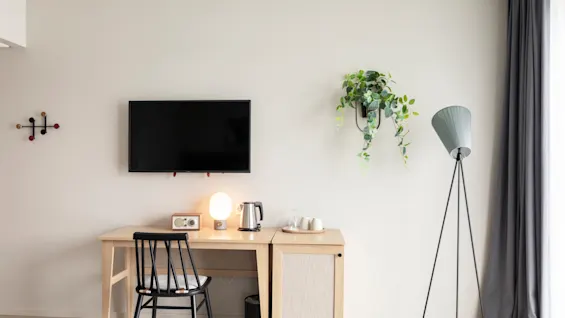 Moderni ja kutsuva huonejärjestely, jossa on puinen työpöytä, televisio ja mukava tuoli, täydennettynä kasvilla ja lampulla.