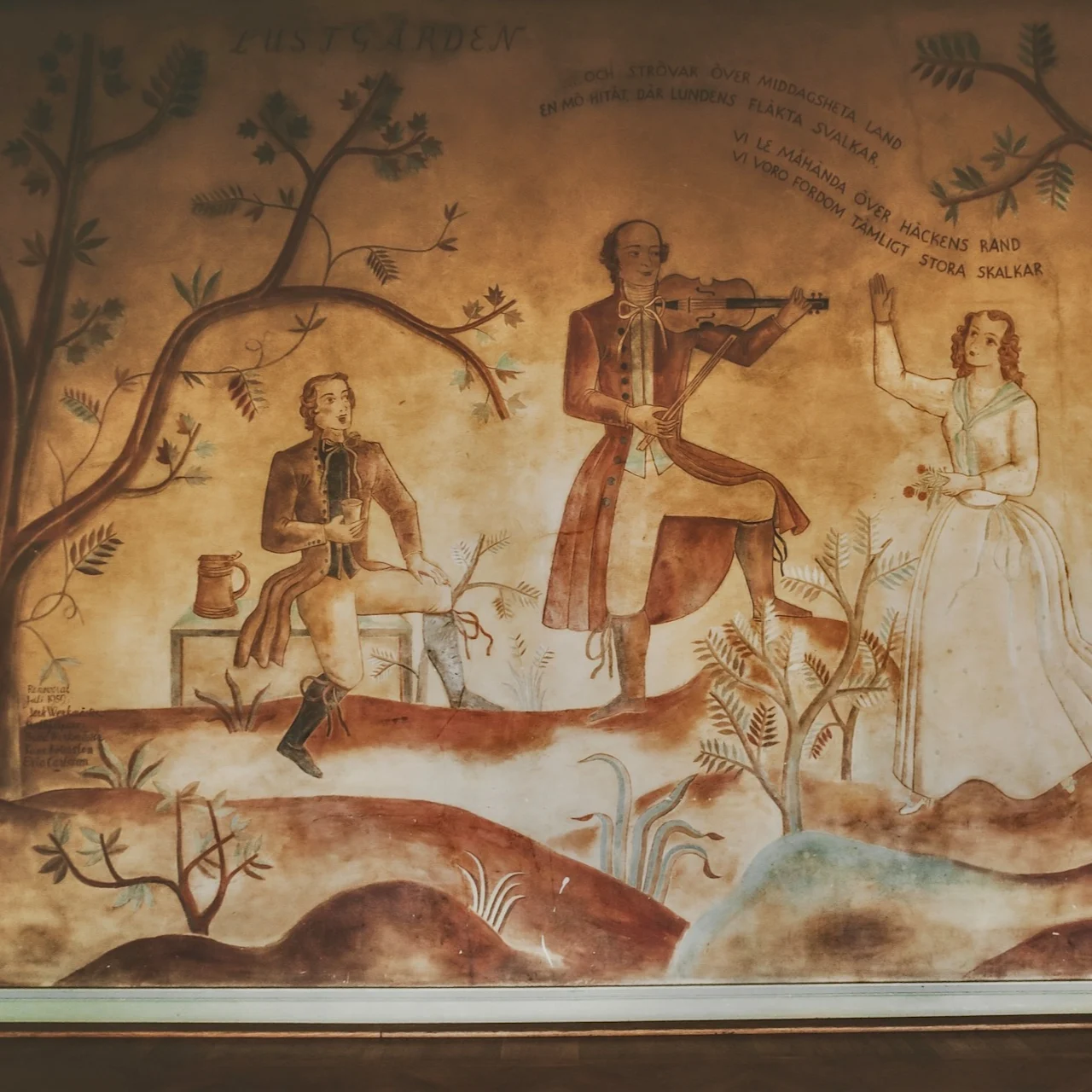 Mural depicting three figures among trees. A man plays a violin, another man sits holding a cup, and a woman stands with flowers. Text: "LUSTGÅRDEN... strövar över middagsheta land..."