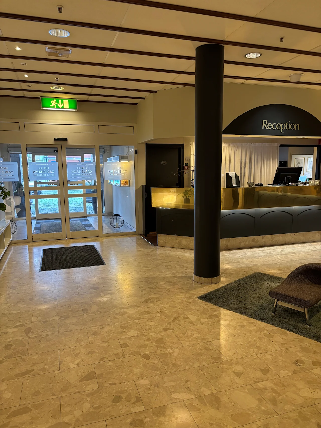 Ljus hotellobby med en reception och entredorrar i glas