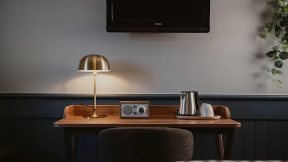 Ett hotellrumsskrivbord med en TV monterad ovanför, med en varm lampa, radio, vattenkokare och koppar för en bekväm vistelse.