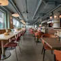 Et moderne og indbydende restaurantinteriør med borde, stole og båse langs store vinduer. En receptionsdisk er synlig.