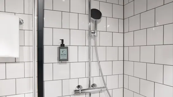 A chrome showerhead and "Hair & Body" dispenser are mounted on white tiled walls. A white towel hangs to the left.