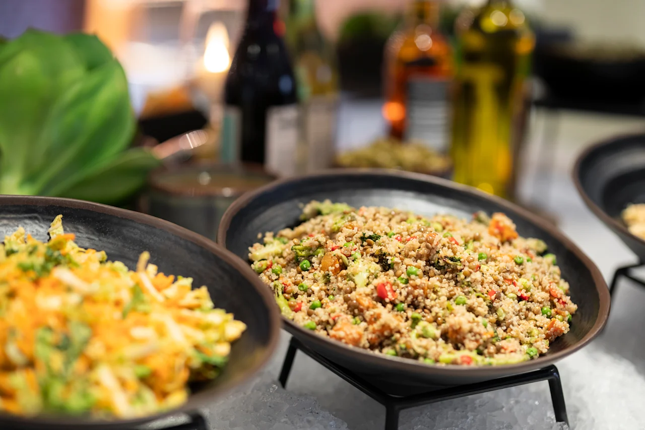 Kaksi kulhoa tuoreita, värikkäitä viljasalaatteja buffetissa, jäähdytettynä jäällä, taustalla sumeita pulloja.