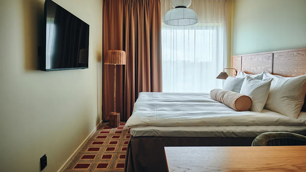 Et koselig hotellrom med en stor seng, en veggmontert TV og varm belysning, klart for et komfortabelt opphold.