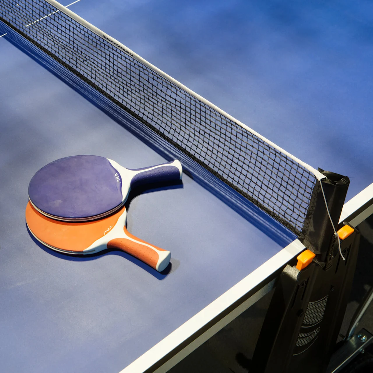 Ping pong paddles rest on a blue table, accompanied by a ball near the net.