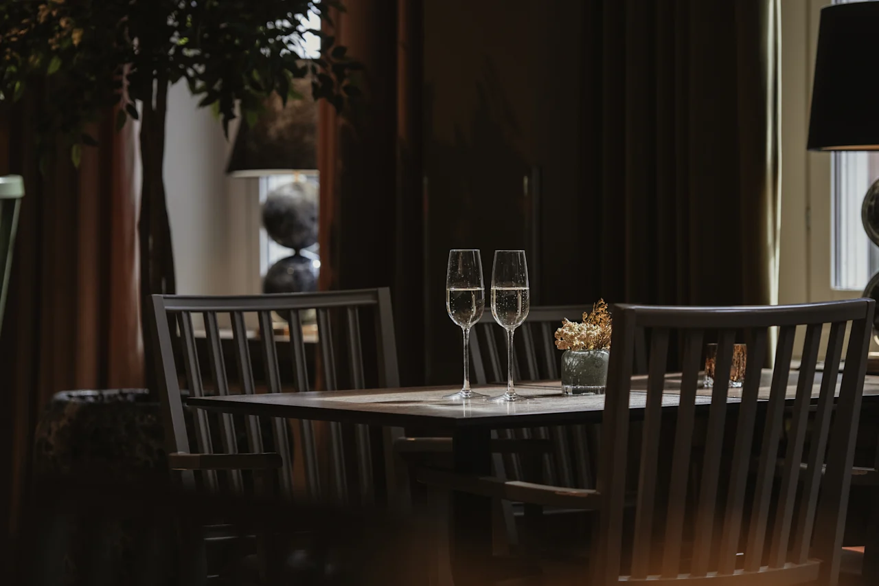 To champagneglass på et bord i et dempet, elegant rom, klart for en feiring eller intim sammenkomst.