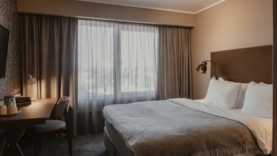 Et komfortabelt hotellrom med en seng, et skrivebord og et stort vindu, som antyder et avslappende opphold.