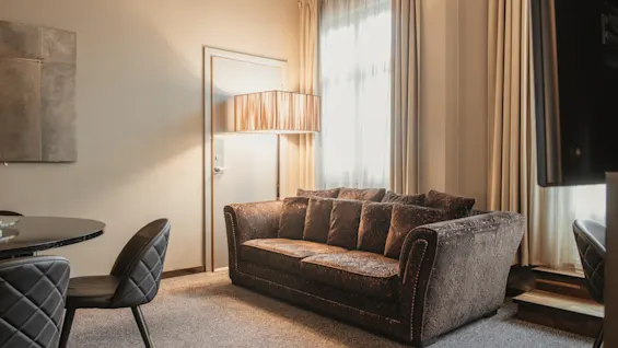 A cozy hotel room with a comfortable sofa, a dining area, and soft lighting.