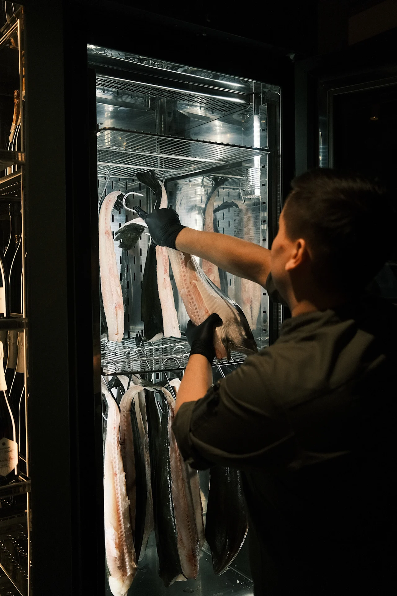En person i sorte handsker arrangerer fiskefileter i en køler på Sjøbua, Hotel Brosundet i Ålesund.