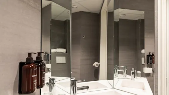 Ett modernt och rent badrum med dubbla handfat, eleganta kranar och flera speglar, med toalettartiklar prydligt arrangerade.