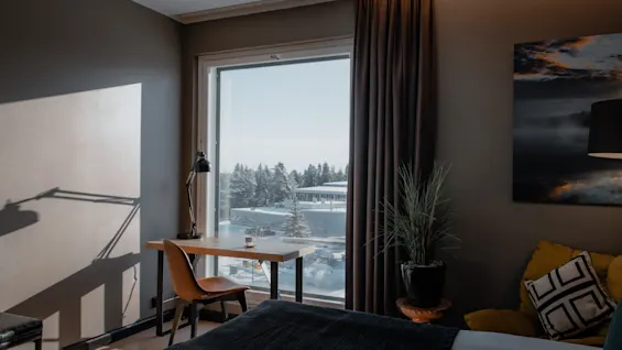 Hotellrom med skrivebord ved stort vindu, utsikt over snødekt landskap og trær. Koselig og lyst rom.