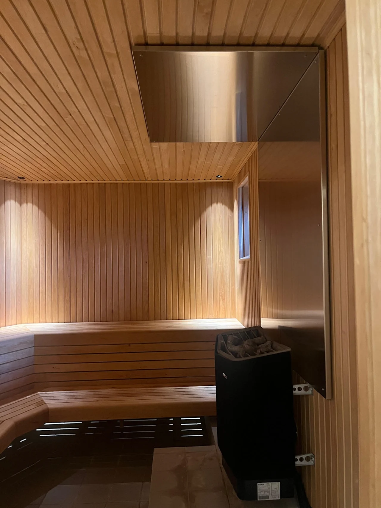 Et varmt, innbydende badstuerom med trebenker og vegger, med en varmeovn og myk belysning. Home Hotel Bilan Wellness.
