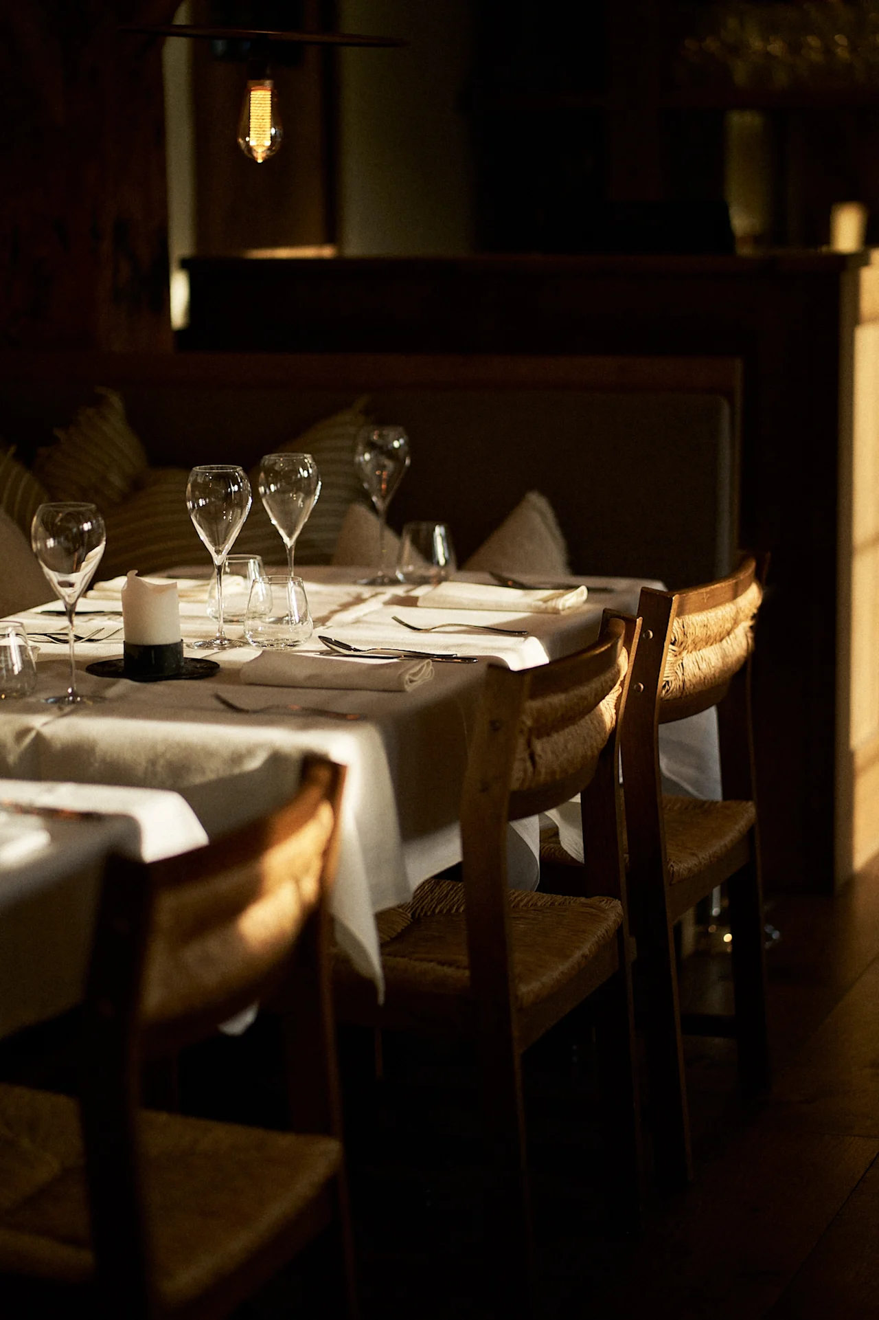 Et smukt dækket spisebord med vinglas, bestik og et stearinlys, badet i varmt sollys på Sjøbua, Hotel Brosundet.