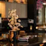 En koselig borddekking i en restaurant eller bar, med en dekorativ plante i en svart og gullfarget vase, en liten gullpotte og bøker.