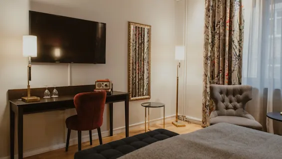 A welcoming hotel room at Home Hotel Kung Oscar featuring a comfortable bed, a work desk with a TV, and elegant decor.