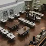 Borden är arrangerade med vaser ovanpå i en rymlig, väl upplyst matplats med grön och vit inredning. Trappor leder uppåt. Skyltar lyder: "Cafeteria, Talk About Your Dreams," "Welcome Lounge."