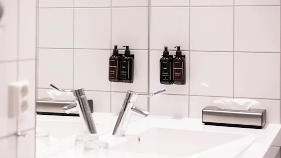 Moderne badeværelse med to håndvaske, vandhaner og vægmonterede dispensere: SHAMPOO, CONDITIONER, SOAP, BODY LOTION.