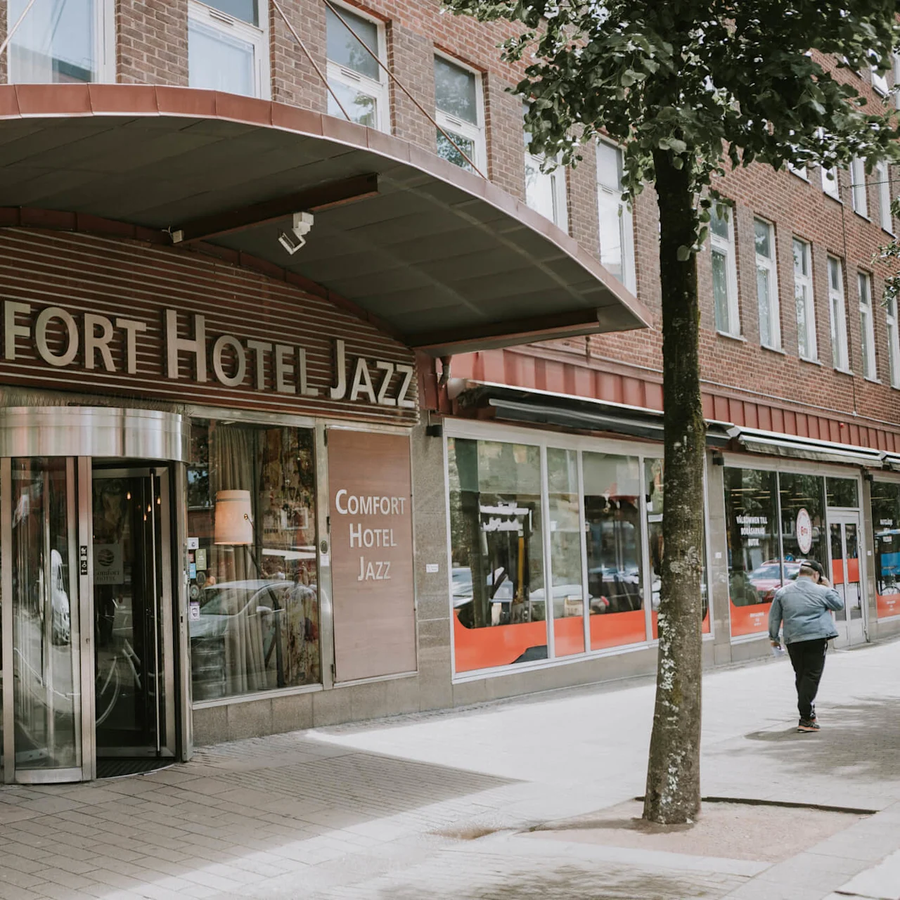 En hotelindgang med en roterende dør og et skilt, der står "COMFORT HOTEL JAZZ" i en bymæssig sammenhæng.