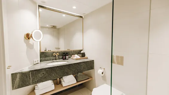 Modernt hotellbadrum med elegant marmorhandfat, stor spegel och ljus belysning.