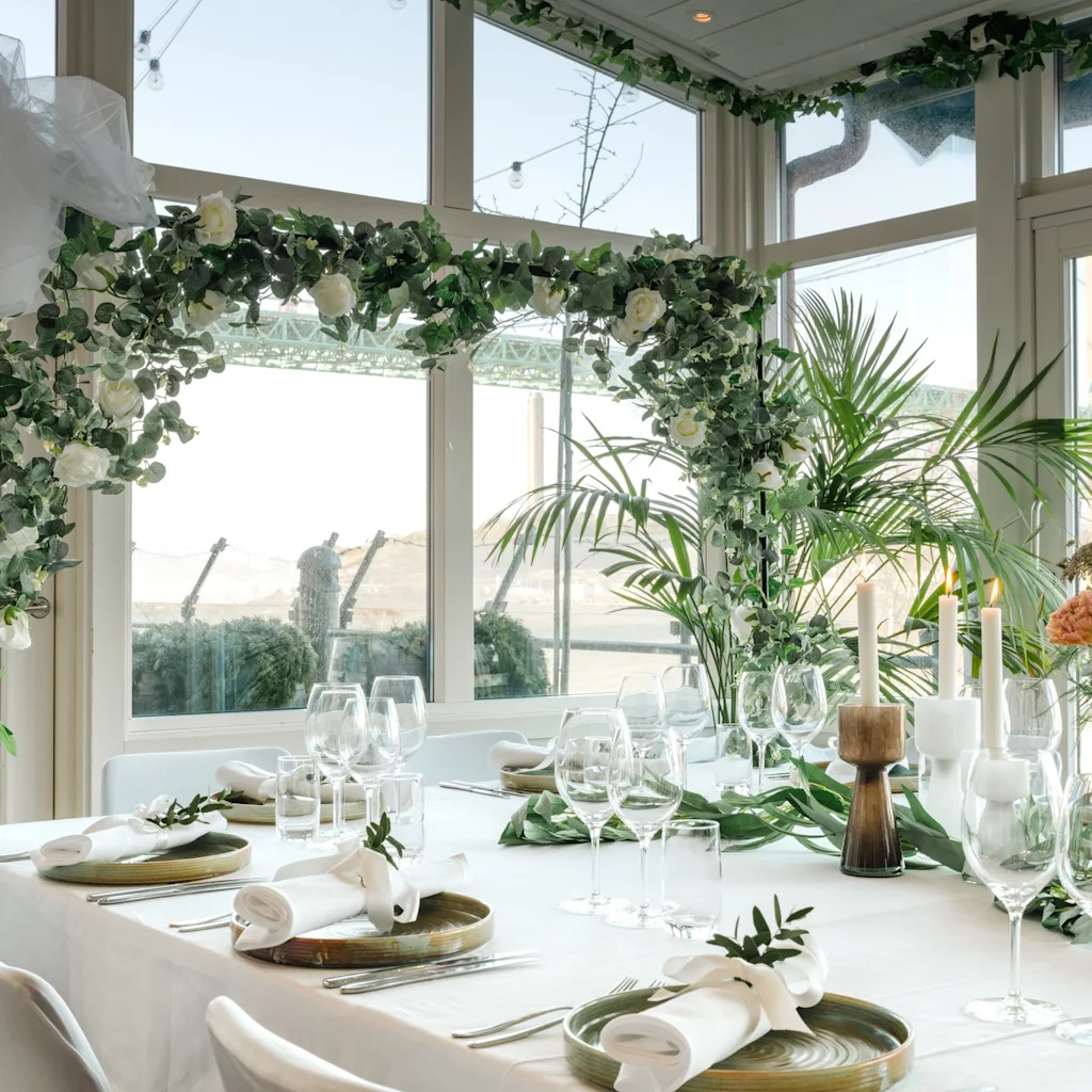 Ett vackert dukat bord för ett speciellt evenemang, med vita blommor, frodig grönska, levande ljus och eleganta kuvert.