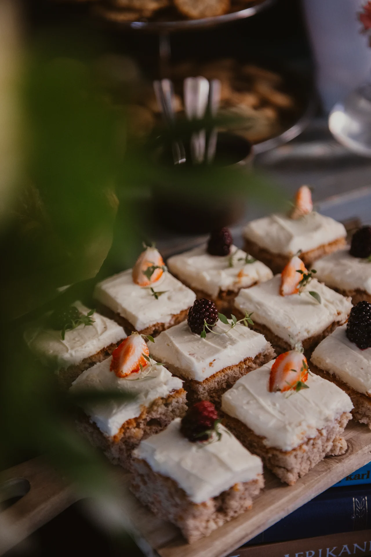 A delightful spread of small cakes with white frosting, fresh berries, and herbs on a wooden board at Home Hotel Uppsala. AMERIKAN.
