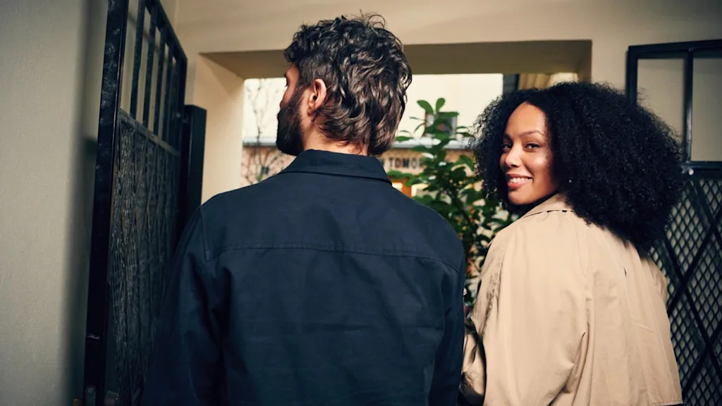 En mann og en kvinne går, kvinnen smiler tilbake mot kameraet. Synlig tekst: TOMOR.