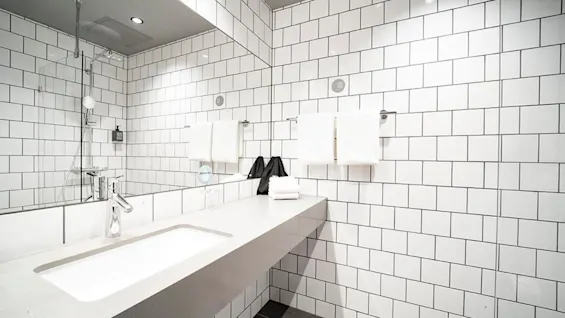A clean, modern bathroom with white subway tiles, a sink, mirror, and shower. Fresh towels are neatly folded, and a sign reads 'MAKE A DIFFERENCE'.