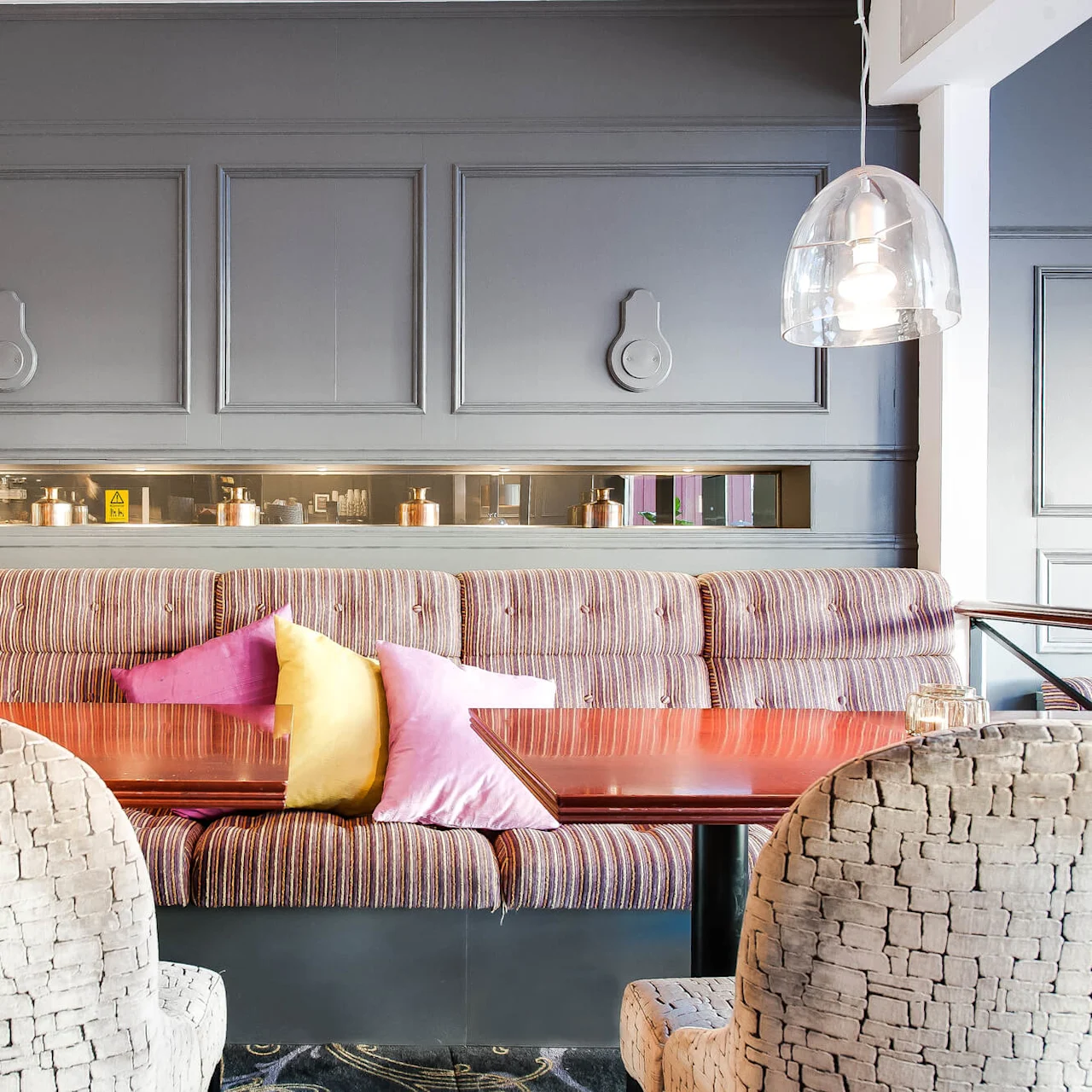 Elegant interiør av en restaurant med stripete sofaer, serveringsvindu og moderne belysning.
