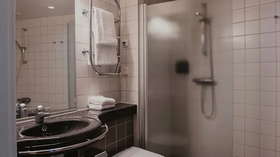 A contemporary bathroom at Home Hotel Uppsala, offering a refreshing shower experience, a sleek sink, and soft towels.