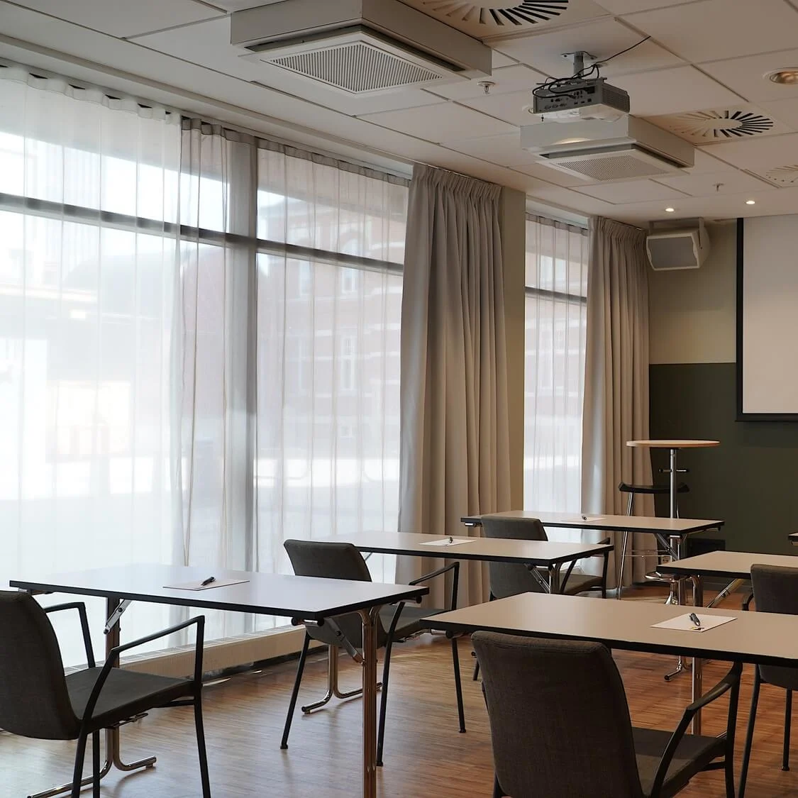 Tables and chairs arranged for a meeting or seminar in a bright room with a projector, screen, and flipchart.