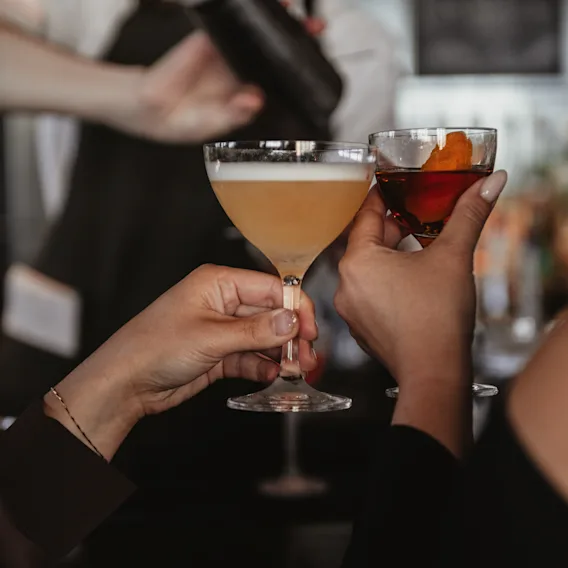Enjoying cocktails at a bar, with a bartender expertly shaking a drink in the background.