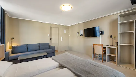 Lyst og moderne hotellrom med dobbeltseng, sofa og skrivebord.