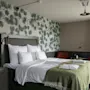 Kutsuva hotellihuone, jossa on mukava sänky vihreällä peitolla, männynoksatapetti ja oleskelualue.