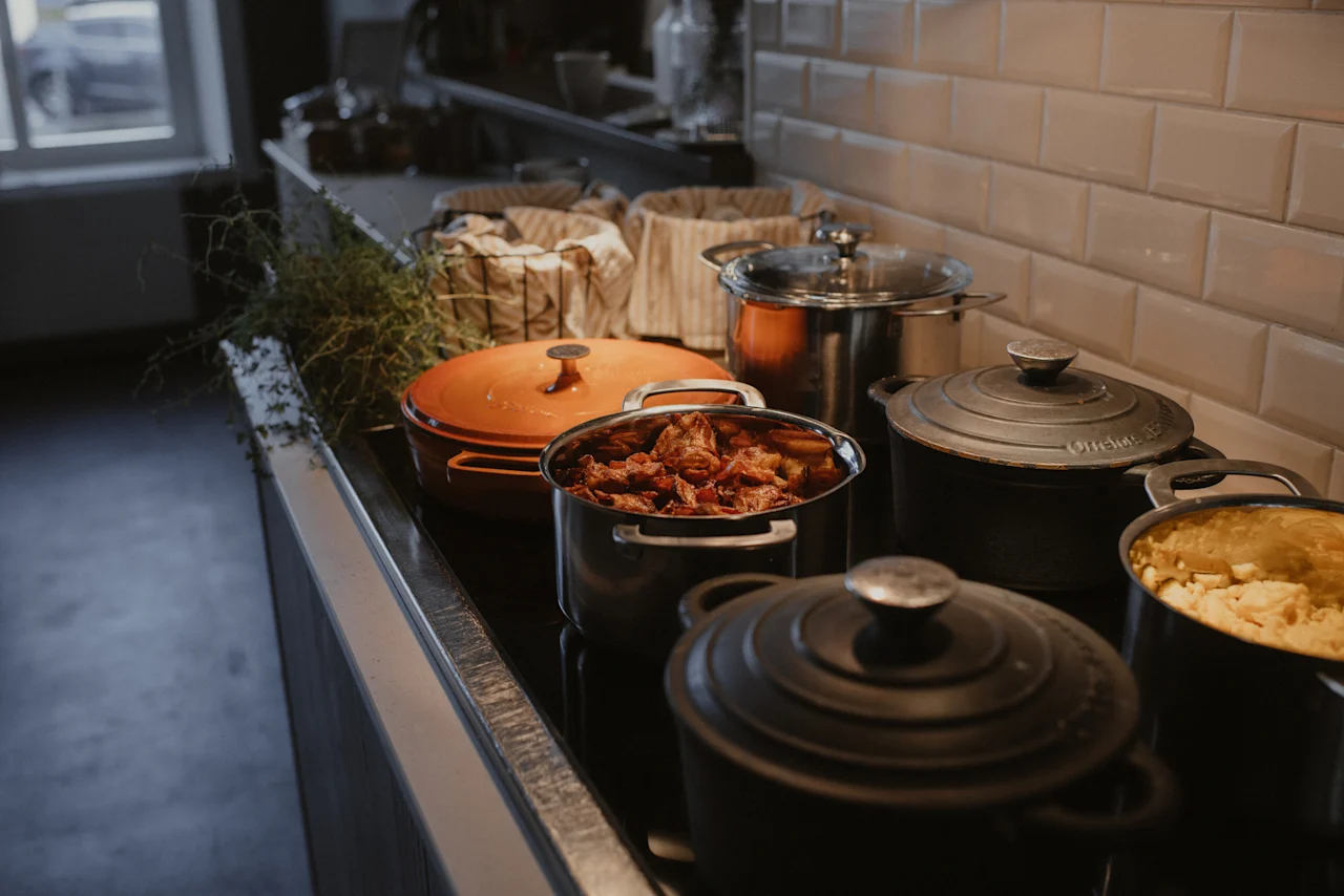 Kastruller och pannor med olika rätter som tillagas eller hålls varma på en spishäll i en hotellköksmiljö.