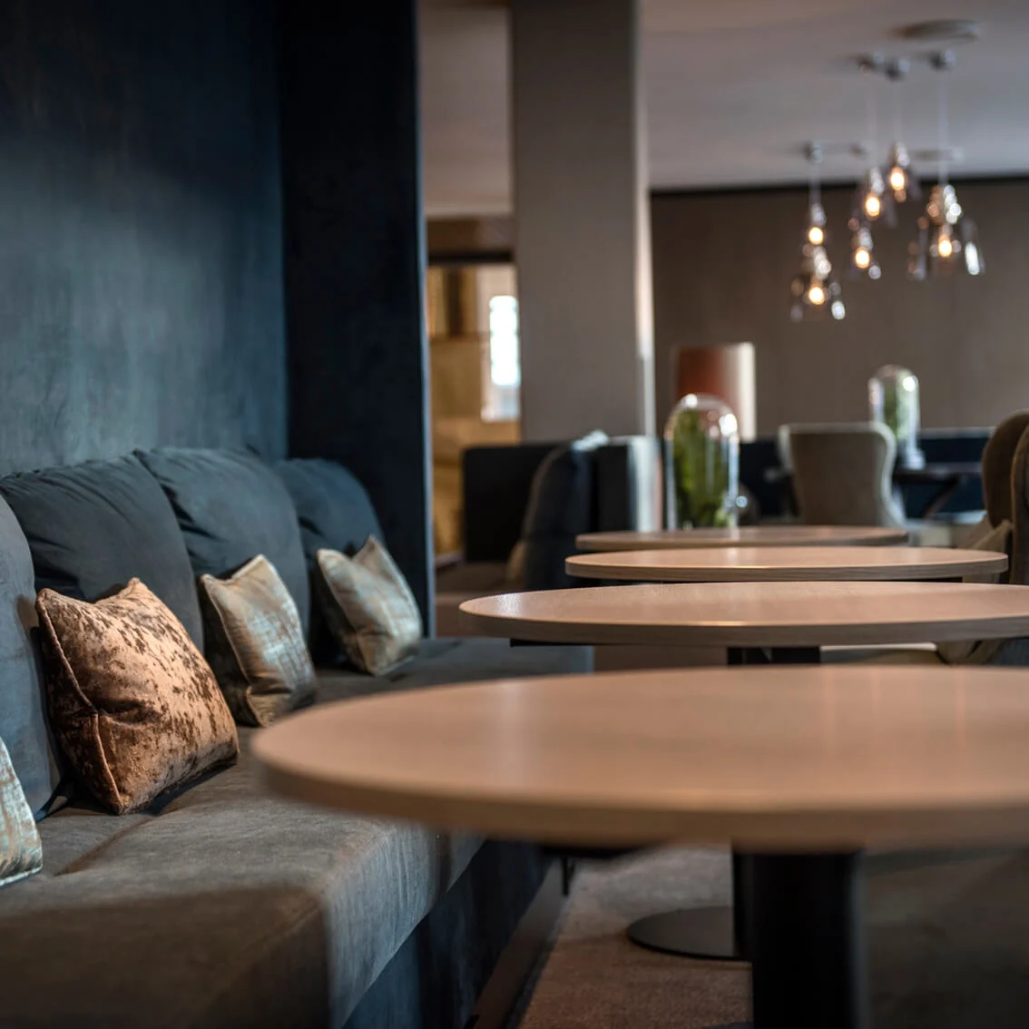 Elegant väntrum med bekväm grå soffa och dekorativa kuddar, runda träbord; modern och mysig inredning.