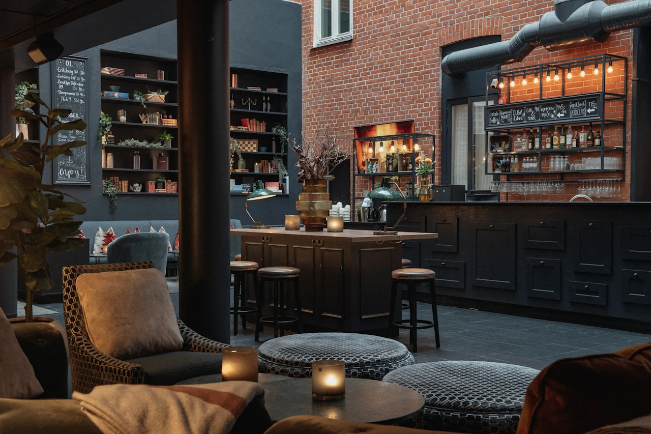 En hyggelig hotellounge med bar, komfortable siddepladser og hylder. En tavle siger Enjoy og en menu viser forskellige drinks.