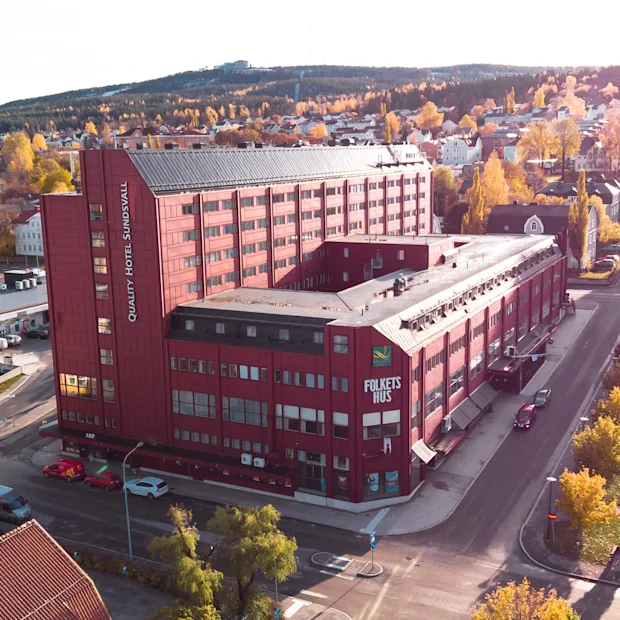 Luftfoto af en efterårsby med en stor rød bygning mærket HOTEL SUNDSVALL og FOLKETS HUS, omgivet af gule træer.