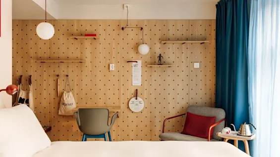 A modern hotel room at hobo oslo with a pegboard wall, desk, armchair, and a tea/coffee station. Visible text: steamer bag, to know more ask us, scan me.