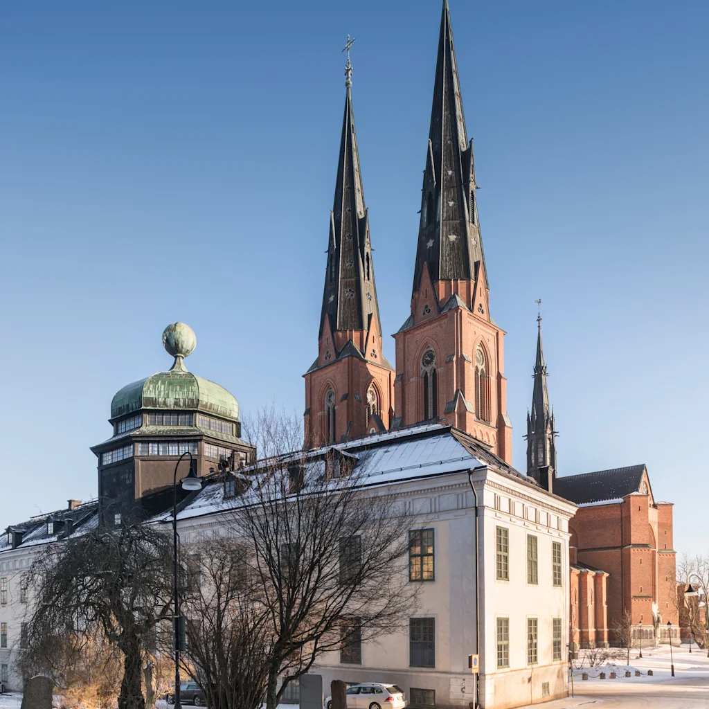 En snöig gatubild i Uppsala med Gustavianum-byggnaden och en stor katedral med dubbla spiror under en klar himmel.