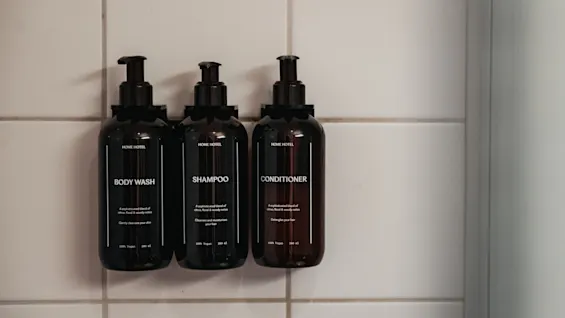 Three dark bottles of body wash, shampoo, and conditioner are mounted on a tiled wall in Home Hotel Uppsala.