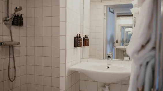 Puhdas ja moderni hotellin kylpyhuone, jossa on suihku annostelijoilla ja pesuallas peilillä ja hygieniatuotteilla.