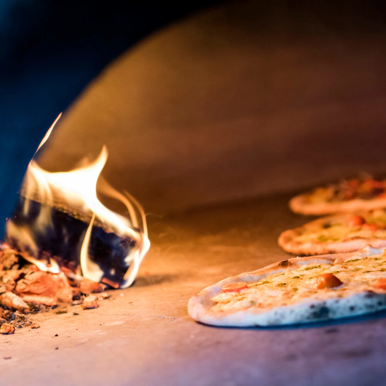 Pizzaer bages i en brændefyret ovn, omkranset af flammer og varme, hvilket skaber en varm, rustik atmosfære.