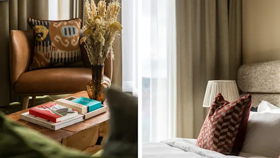 Et stilfuldt hotelværelse med et behageligt siddeområde, inklusive en lænestol og bøger, ved siden af en hyggelig seng med dekorative puder.