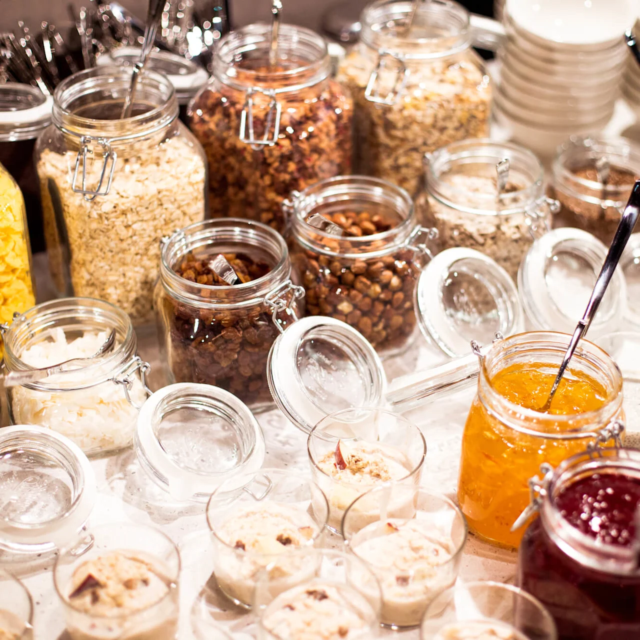 Various jars and bowls filled with breakfast items like cereals and jams are displayed on a table.