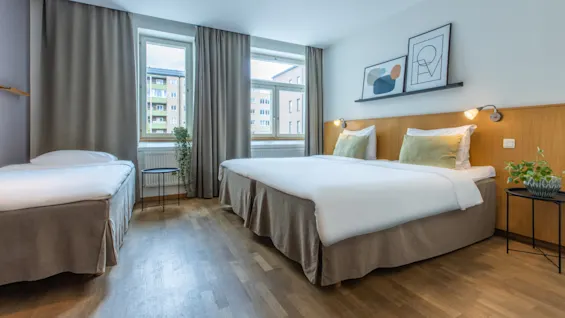 A hotel room with two twin beds, artwork on the wall, and a window revealing an urban view.
