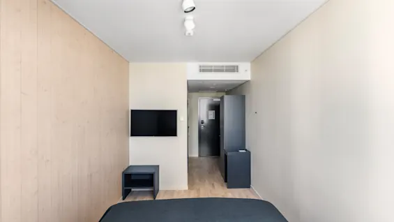 Et moderne og indbydende hotelværelse med en komfortabel seng, et vægmonteret tv og en tydelig indgang.