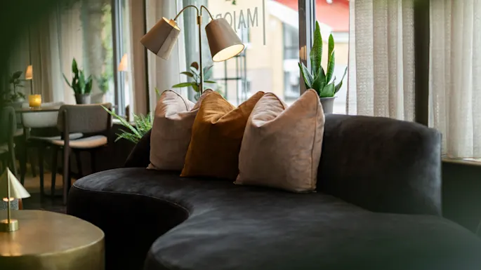 An inviting lounge area with a dark curved sofa, plush pillows, and warm lighting, perfect for relaxation.
