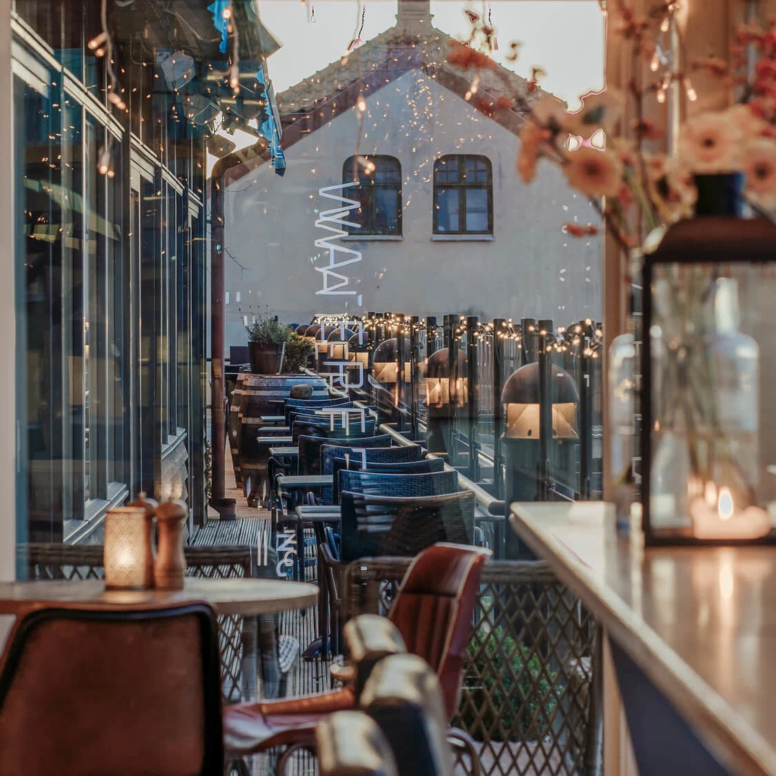 Restaurant interior with candle-lit tables, chairs flanking a windowed walkway adorned with string lights; text reads “WHAT’S FREDERIK INC?”.