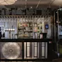 Bar med flaskor och glas uppradade, bakbelysta och organiserade. Svarta tavlan ovan listar drycker och snacks: "RED, WHITE, COCKTAILS 40 kr, SNACKS FROM THE KITCHEN." Elegant interiör med modern inredning.